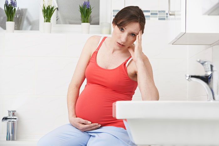 Kobieta w ciąży w ciąży w łazience trzyma się za brzuch i za głowę